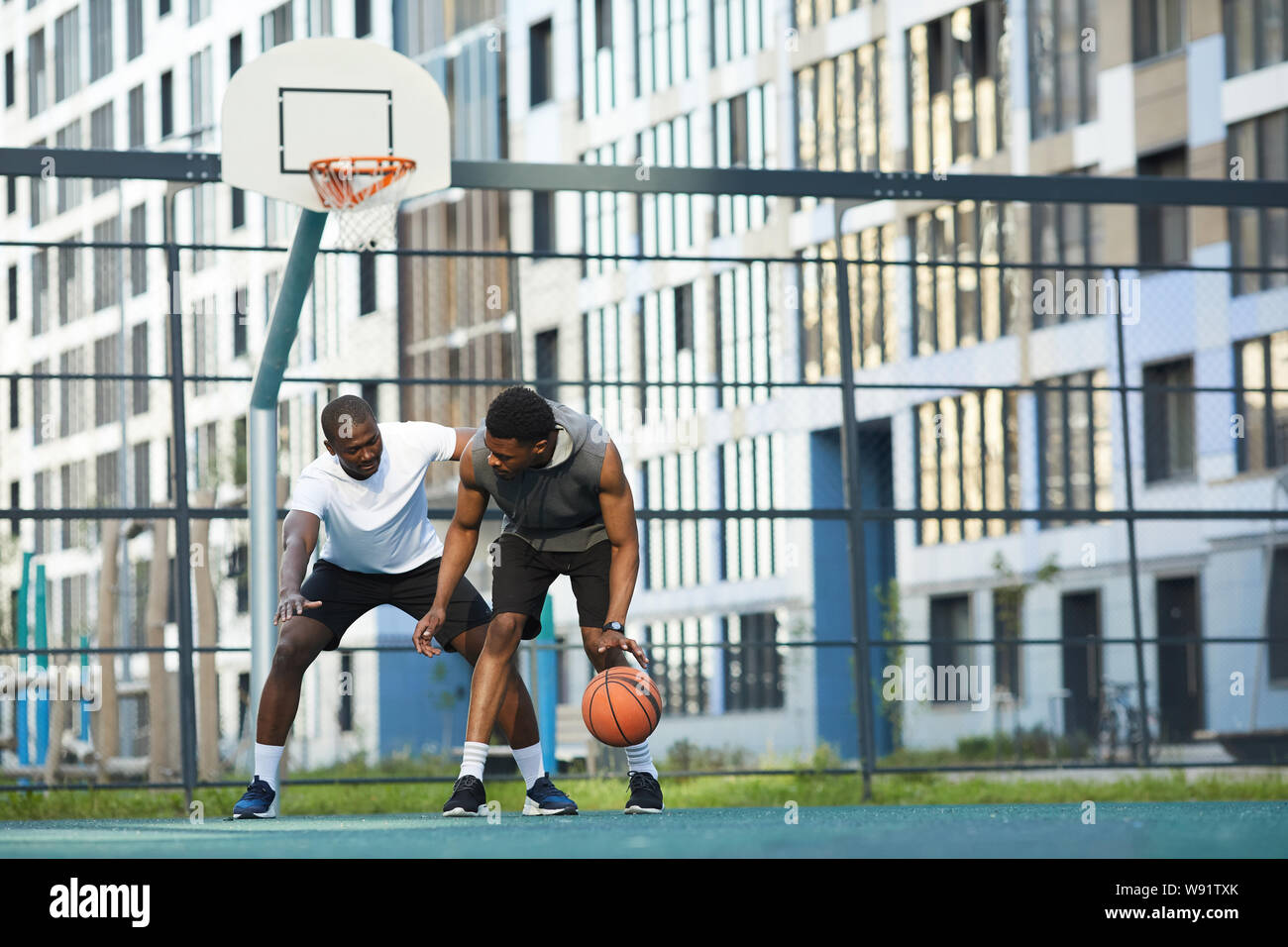 Full length action shot of two African-American guys playing basketball in outdoor court in urban setting, copy space Stock Photo