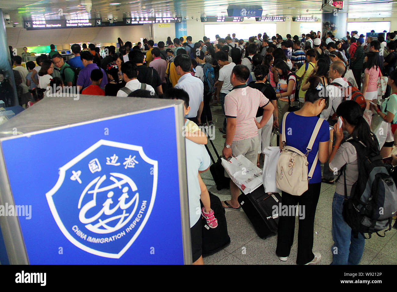 --FILE--Passengers travelling abroad wait to check in next to a signboard of China Immigration Inspection at the Qingdao Liuting International Airport Stock Photo