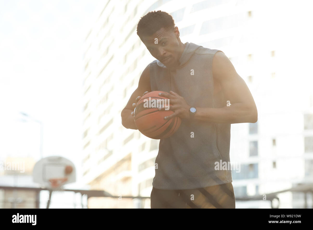Waist up portrait of handsome African man holding ball while standing in basketball court outdoors, copy space Stock Photo