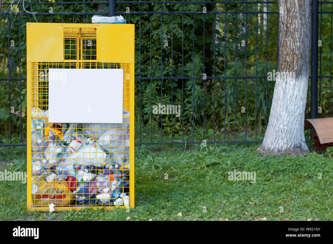 Yellow iron mesh for plastic waste for recycling near green trees in