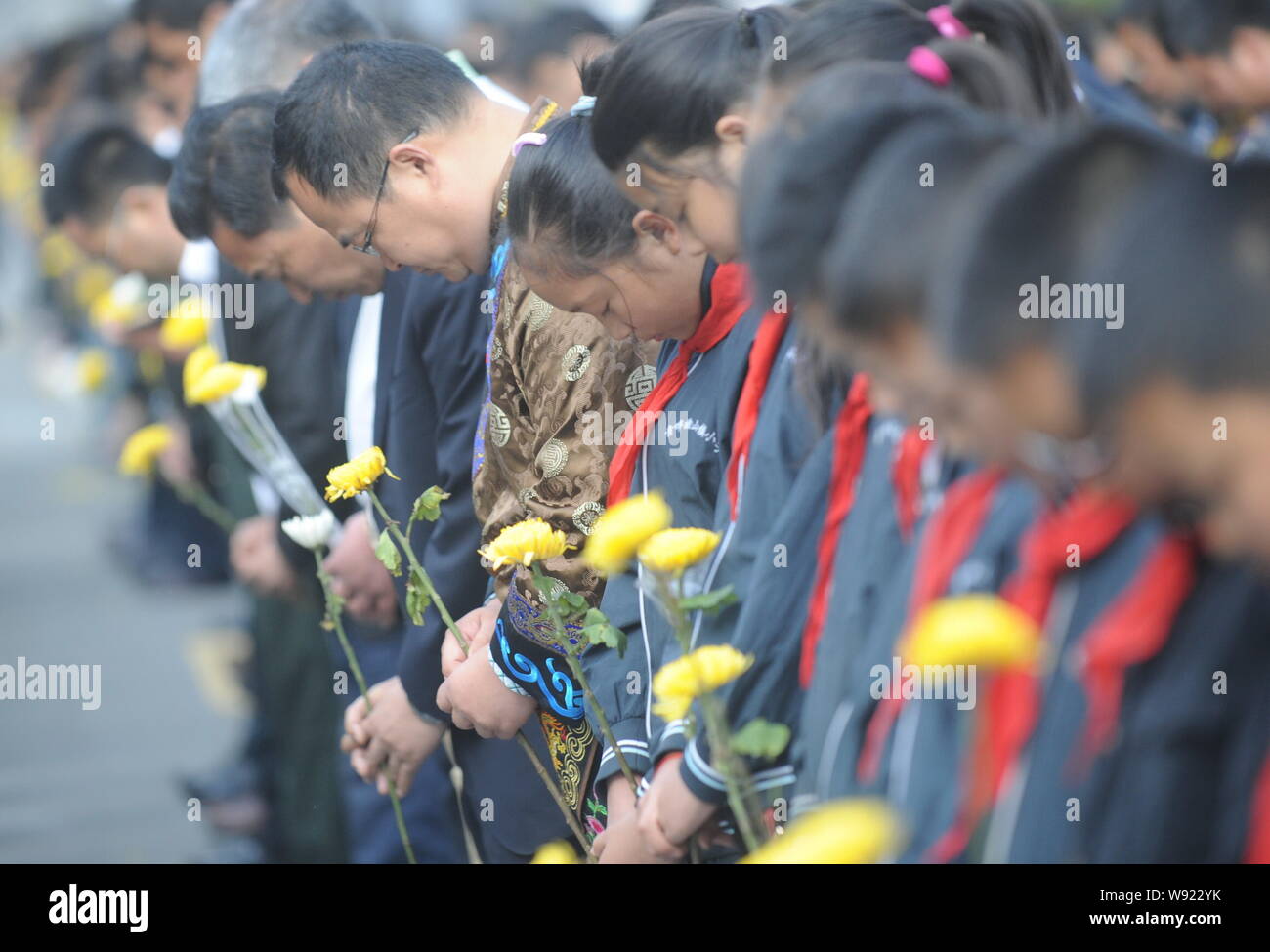 People hold flowers as they observe a minute of silence to mourn the victims of the 7.9-magnitude May 12 Sichuan Earthquake during a public mourning e Stock Photo