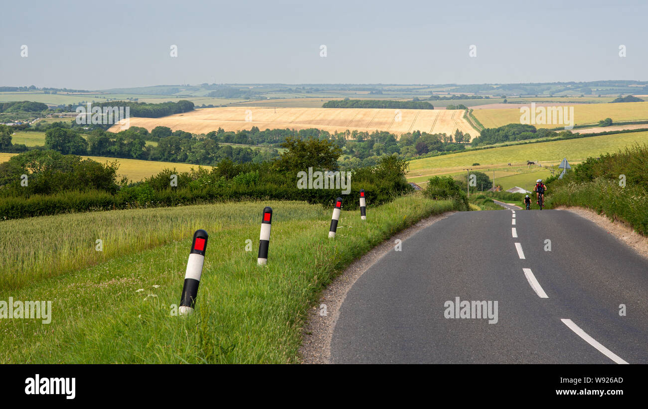 Dorchester, Dorset, UK - June 29, 2019: Two cyclists ride on a country lane in the pastoral landscape of the Dorset Downs hills. Stock Photo