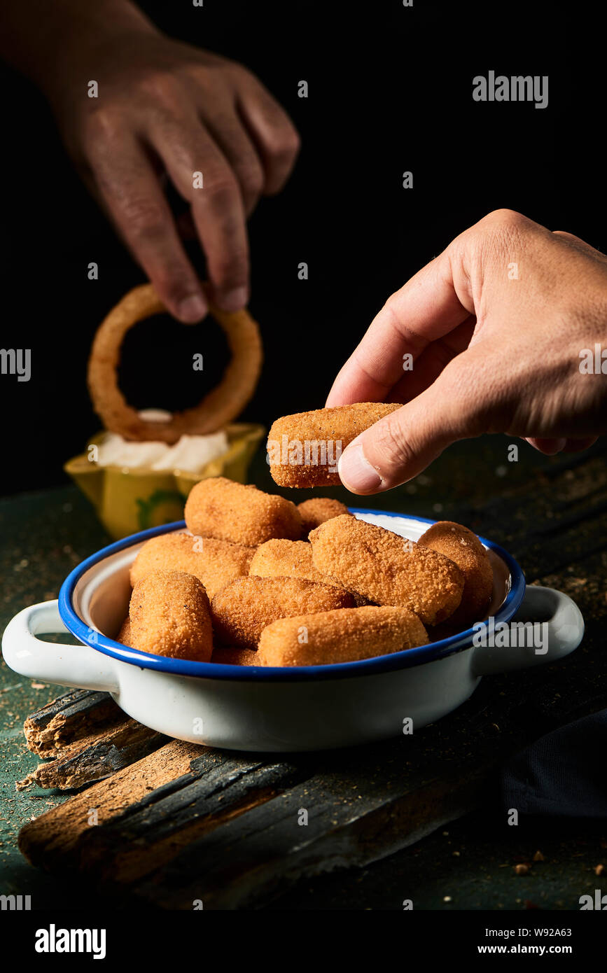 closeup of a man picking a spanish croquette from a white and blue enamel plate, and another man dipping a calamar a la romana, a fried battered squid Stock Photo
