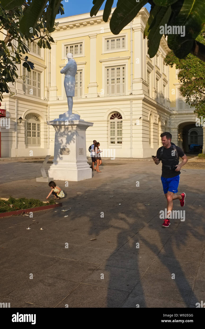 A jogger runs past the Raffles Statue at Raffles' Landing Site by the Singapore River, Singapore, the Museum of Asian Civilizations in the background Stock Photo