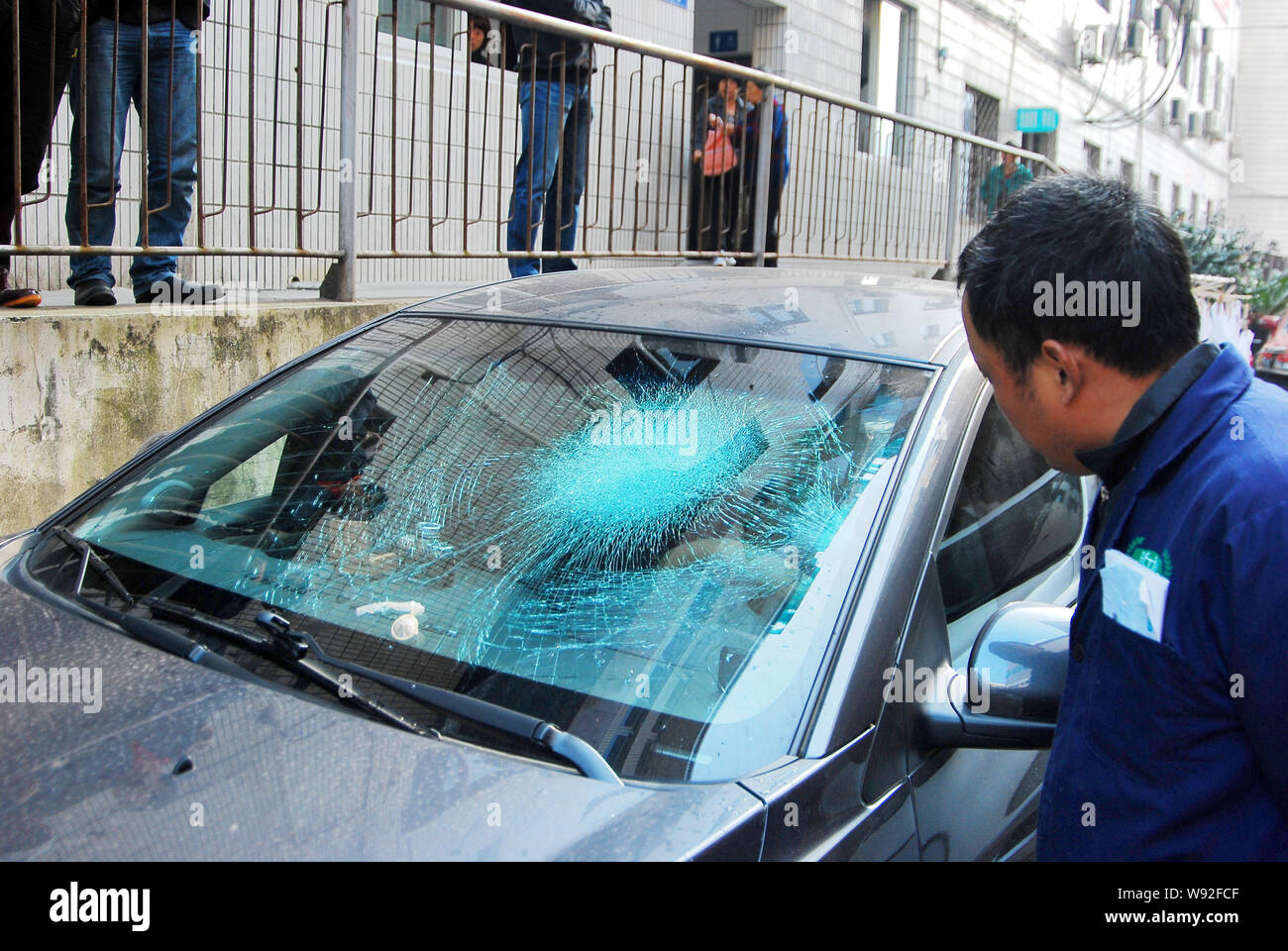 Local residents look at a used condom on the shattered front windshield of a Chevrolet Cruze after it fell from an unknown floor of a high-rise reside Stock Photo
