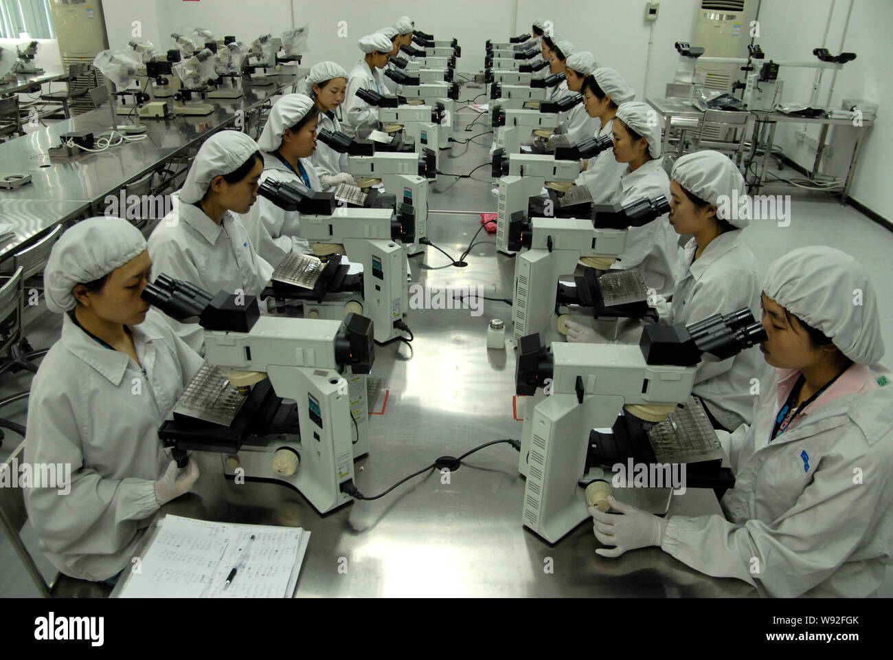 --FILE--Young female Chinese newly-employed workers operate microscopes during a training session at a plant in Dongguan city, south Chinas Guangdong Stock Photo