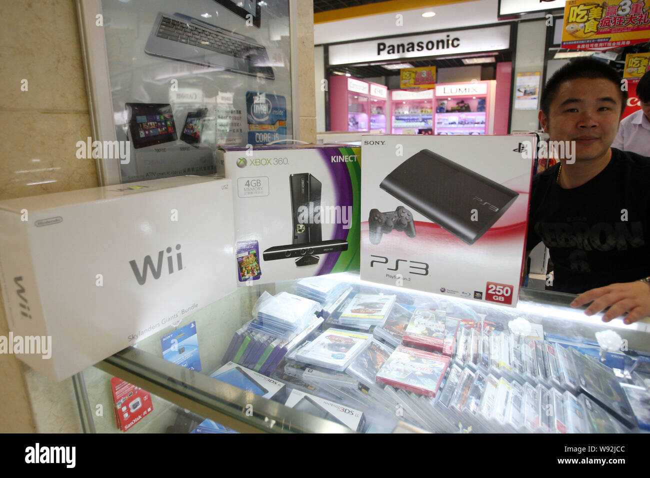 A salesman sells Sony PS3, Microsoft XBOX 360 and Nintendo Wii game consoles at a stall in a digital products mall in Shanghai, China, 10 July 2013. Stock Photo