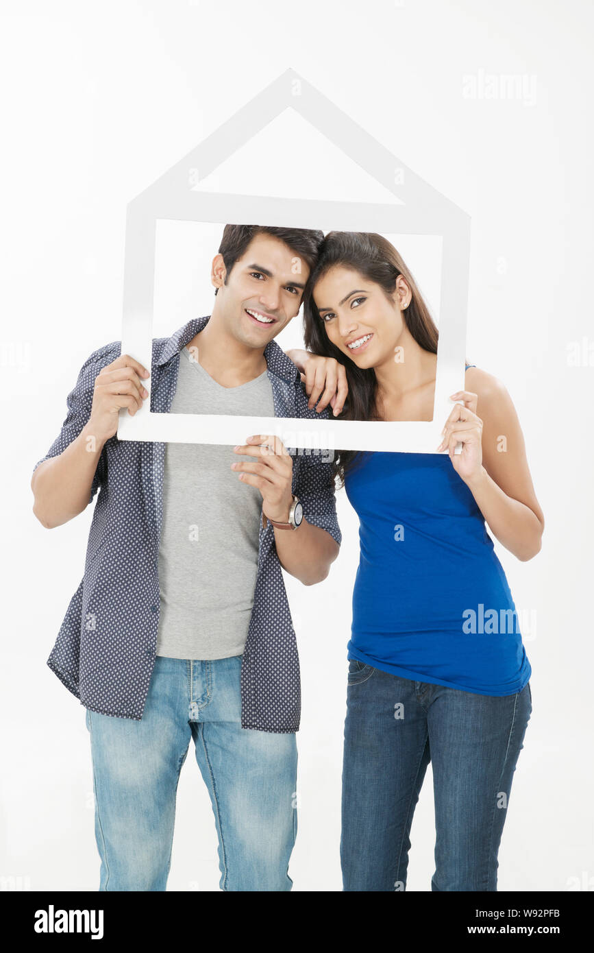 Young couple holding a dream home shape frame Stock Photo - Alamy