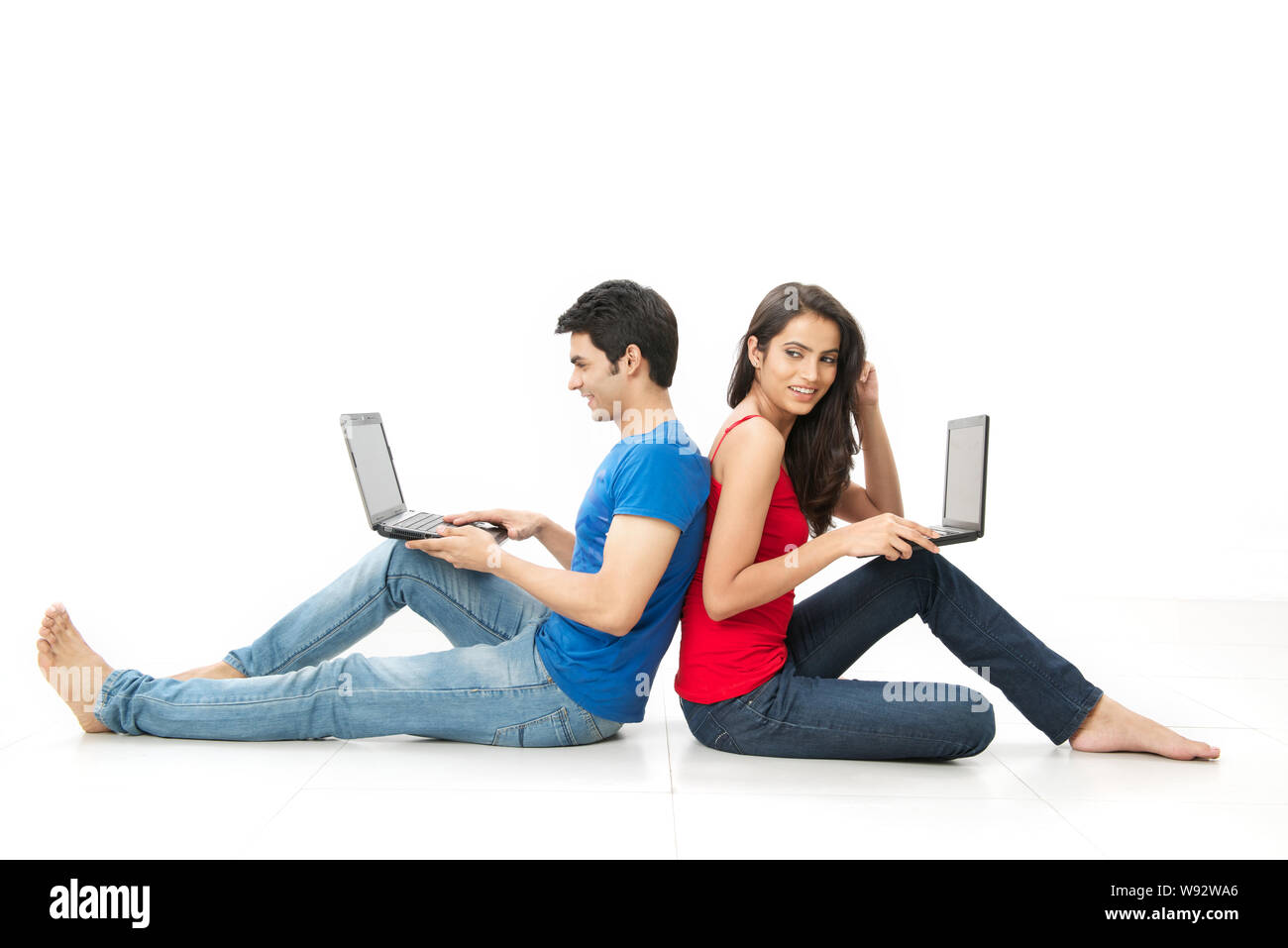 Young couple sitting on floor back to back and using laptops Stock Photo