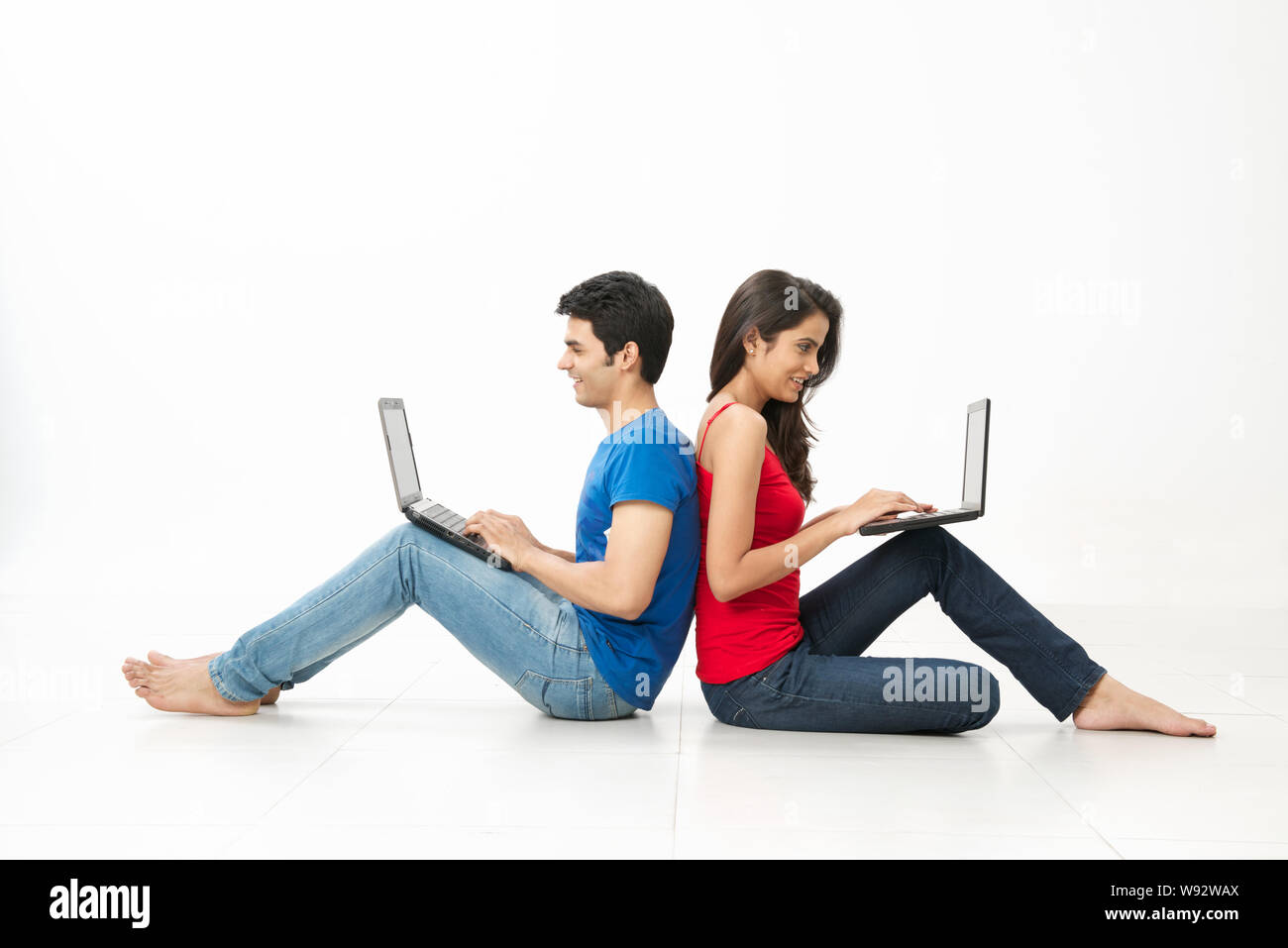 Young couple sitting on floor back to back and using laptops Stock Photo