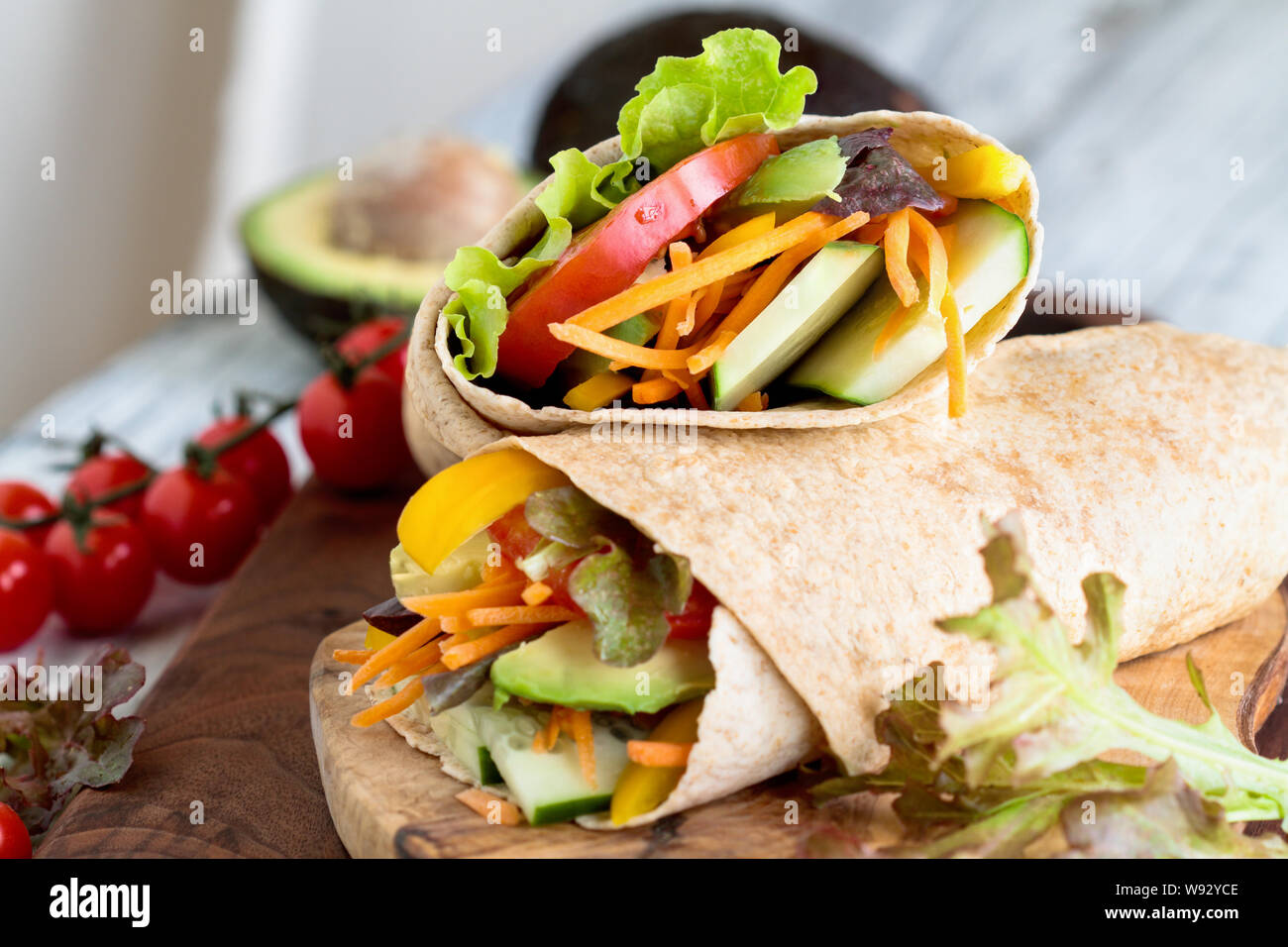 A healthy lunch or dinner of a vegan / vegetarian wrap made with  argula lettuce, sliced tomatoes, cucumbers, avocado, bell peppers and carrots. Stock Photo