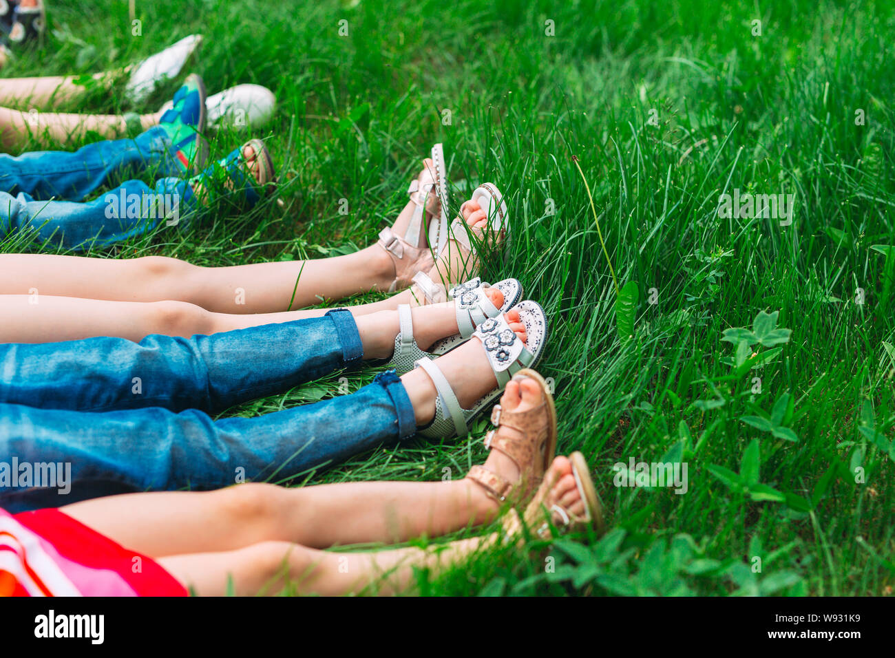 Children lying on green grass in park on a summer day with their legs lifted up to the sky. Stock Photo