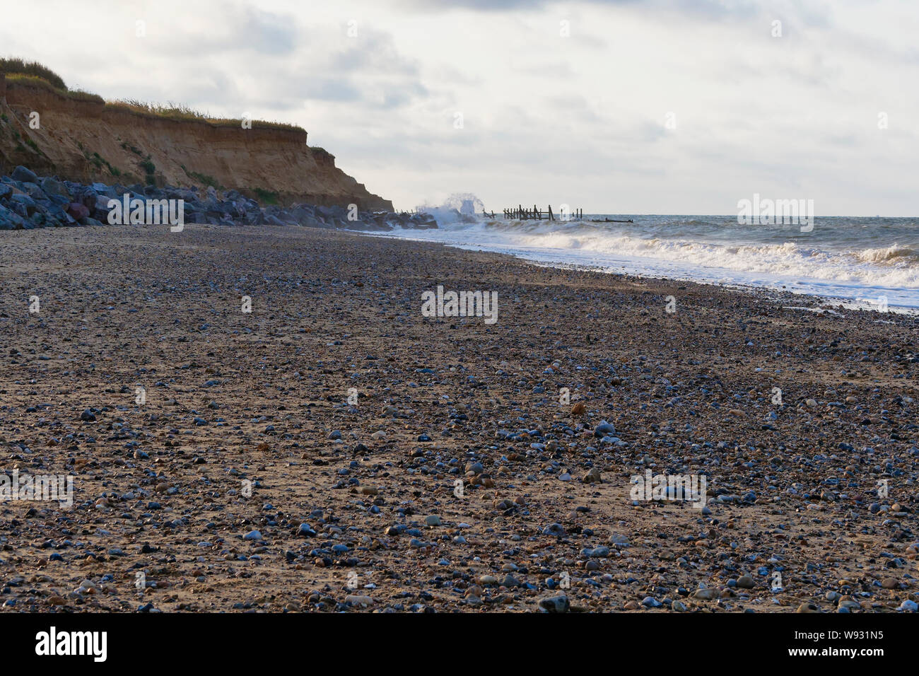 North sea waves break over sea defences protecting the fragils cliffs of Happisburgh beach on a summer evening Stock Photo