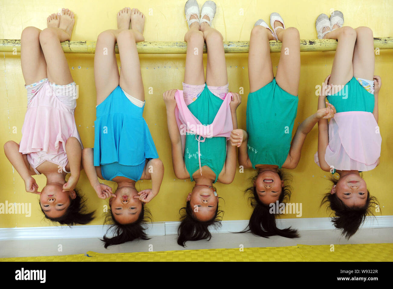 Young Chinese girls smile and make faces as they hang upside down from a ballet barre during a dance training session at a school in Haozhou, east Chi Stock Photo