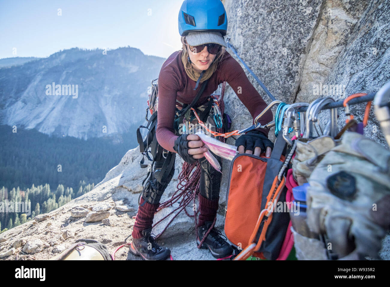 A young woman sorts gear on a spacious ledge during a bigwall climb Stock Photo