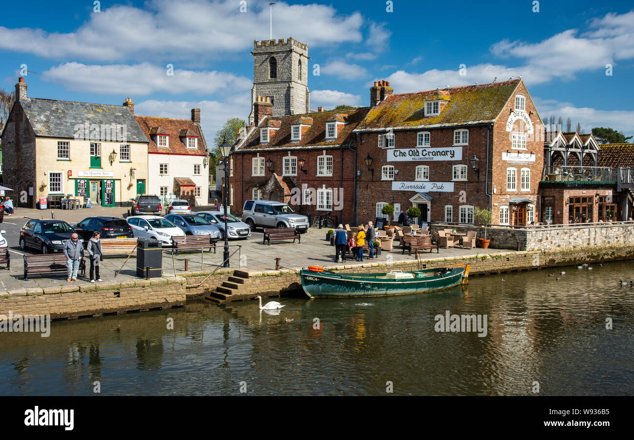 Wareham, England, UK - March 27, 2019: People walk along the Quayside of the River Frome beside the traditional old houses and buildings of Wareham in Stock Photo