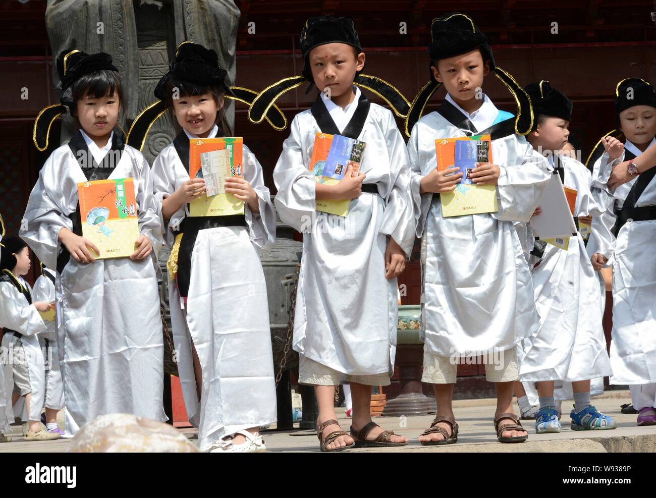 First-grade pupils wearing traditional Chinese uniforms pose with the Analects of Confucius during the first writing ceremony of a new semester at Fuz Stock Photo