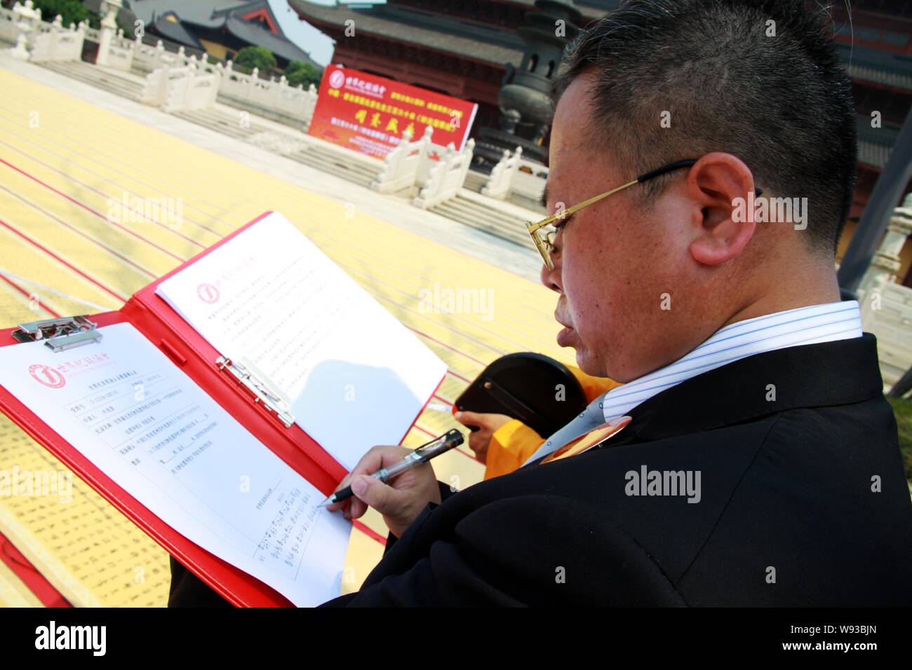 An officer of the World Record Association confirms the length of scrolls of calligraphy named Lotus Sutra created by Ye Zhaojing at Zhongyuan Temple Stock Photo