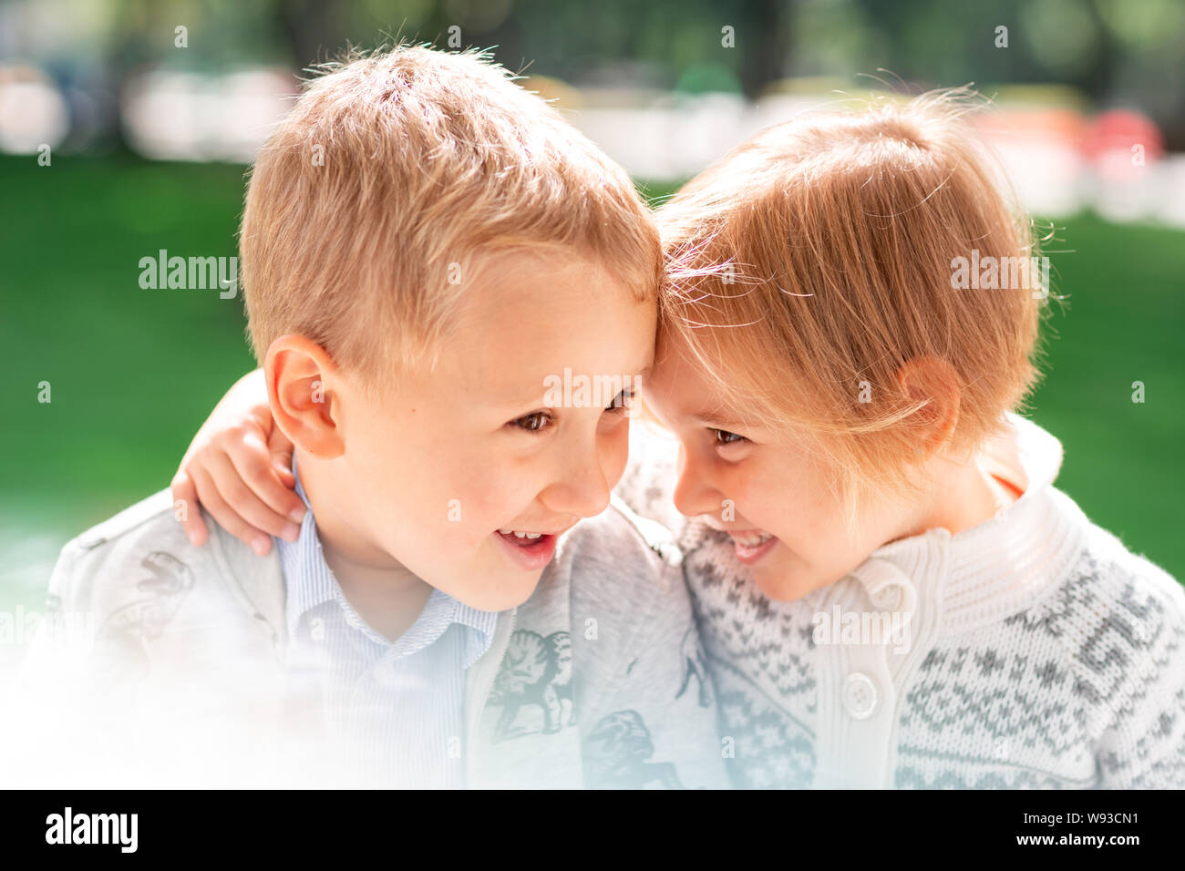 Two happy kids boy and a girl smiling and hugging together in the park ...