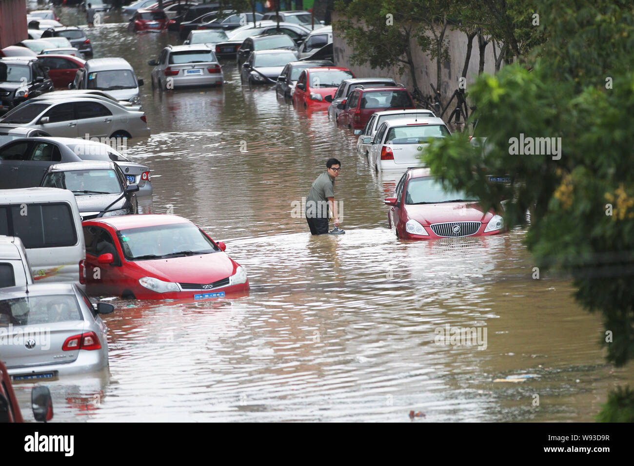 A Chinese man walks past private cars half submerged by floodwaters after heavy rains caused by Typhoon Fitow in RuiAn city, east Chinas Zhejiang prov Stock Photo