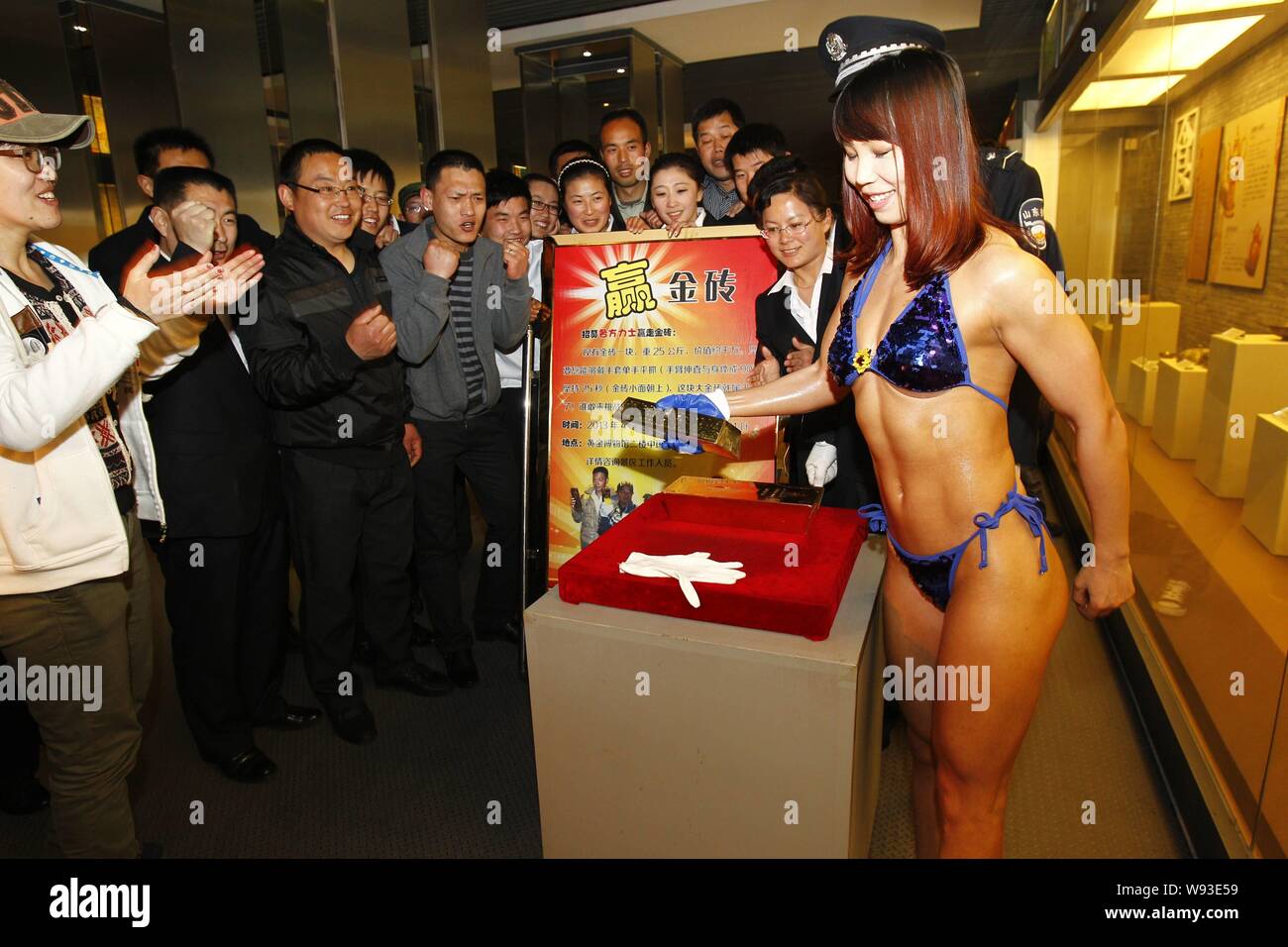 A young woman wearing a bikini tries to snatch up a 12.5kg gold bullion with one hand during a bullion lifting challenge at the China Gold Mining Muse Stock Photo