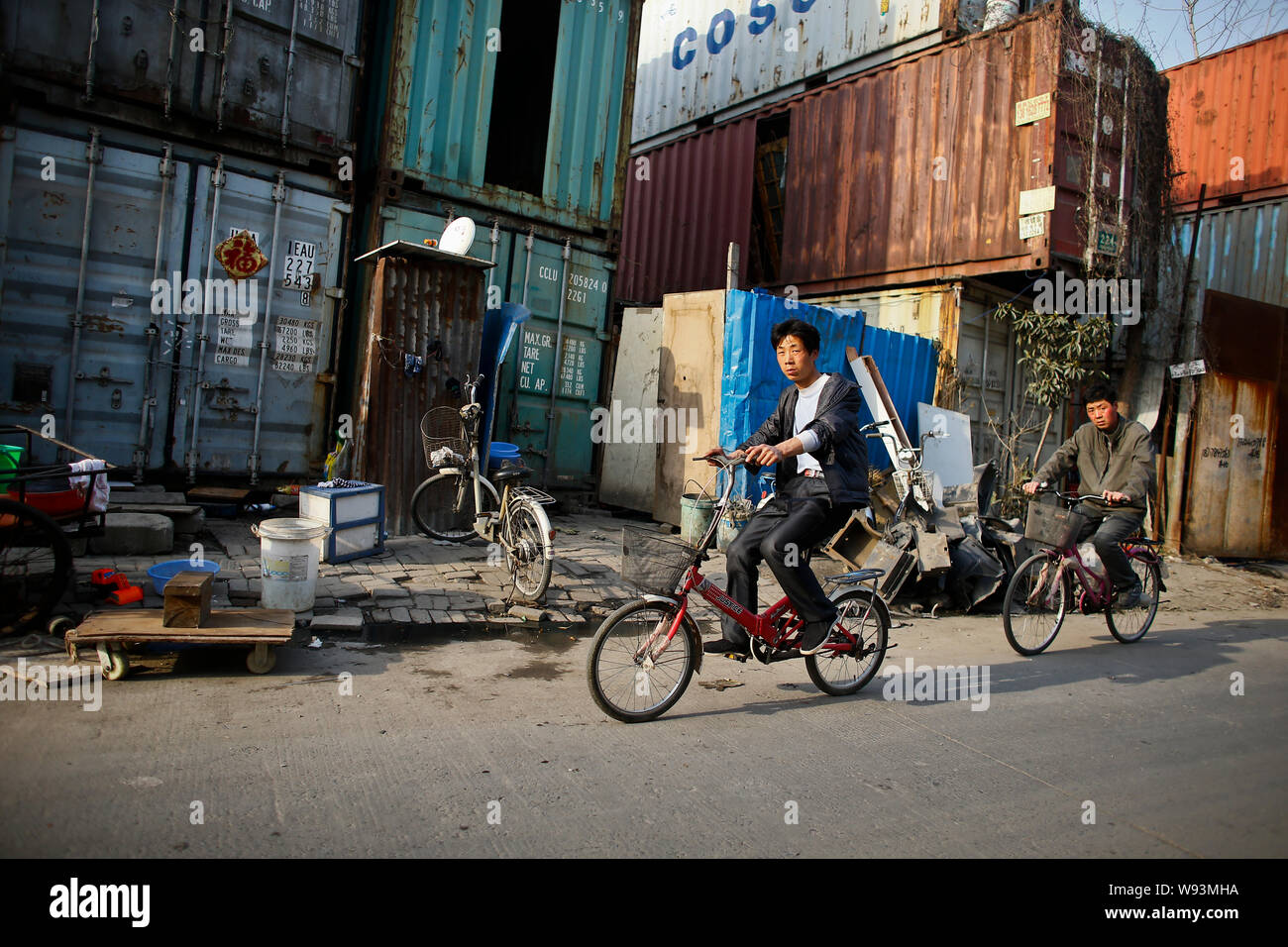 Cyclers drive past homes converted from shipping containers in the suburb of Shanghai, China, 8 March 2013.   People stand outside shipping containers Stock Photo