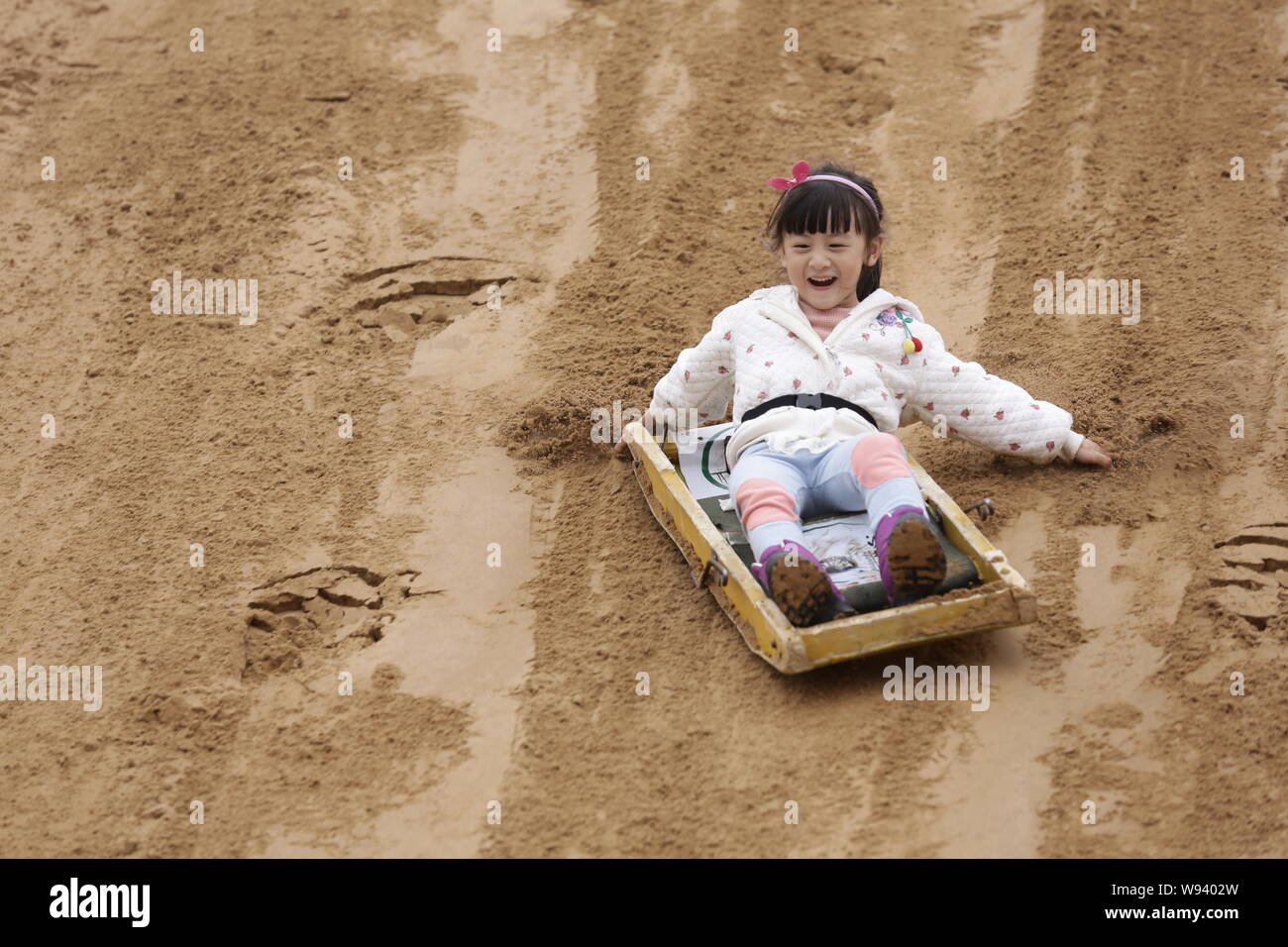 FILE--Cindy Tian Yucheng, the daughter of retired Chinese diver Tian Liang,  has fun with sand sliding during the filming session of an episode of th  Stock Photo - Alamy