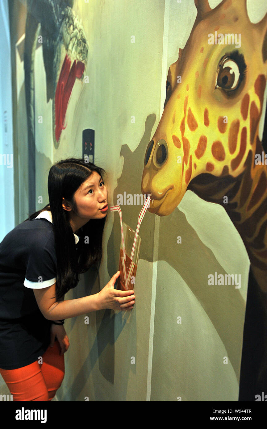 A Chinese girl, left, poses with a 3D painting while mimicking to drink juice at the 3D art experience museum in Wuhan, central Chinas Hubei province, Stock Photo