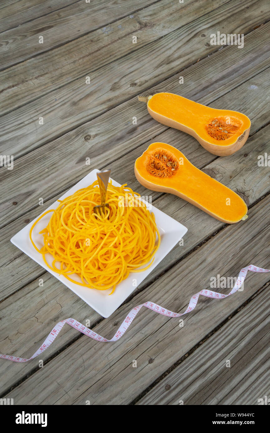 Butternut squash noodles with fork and measuring tape on wooden background. Healthy low carb pasta - new health food trend with vegetable noodle. Grai Stock Photo