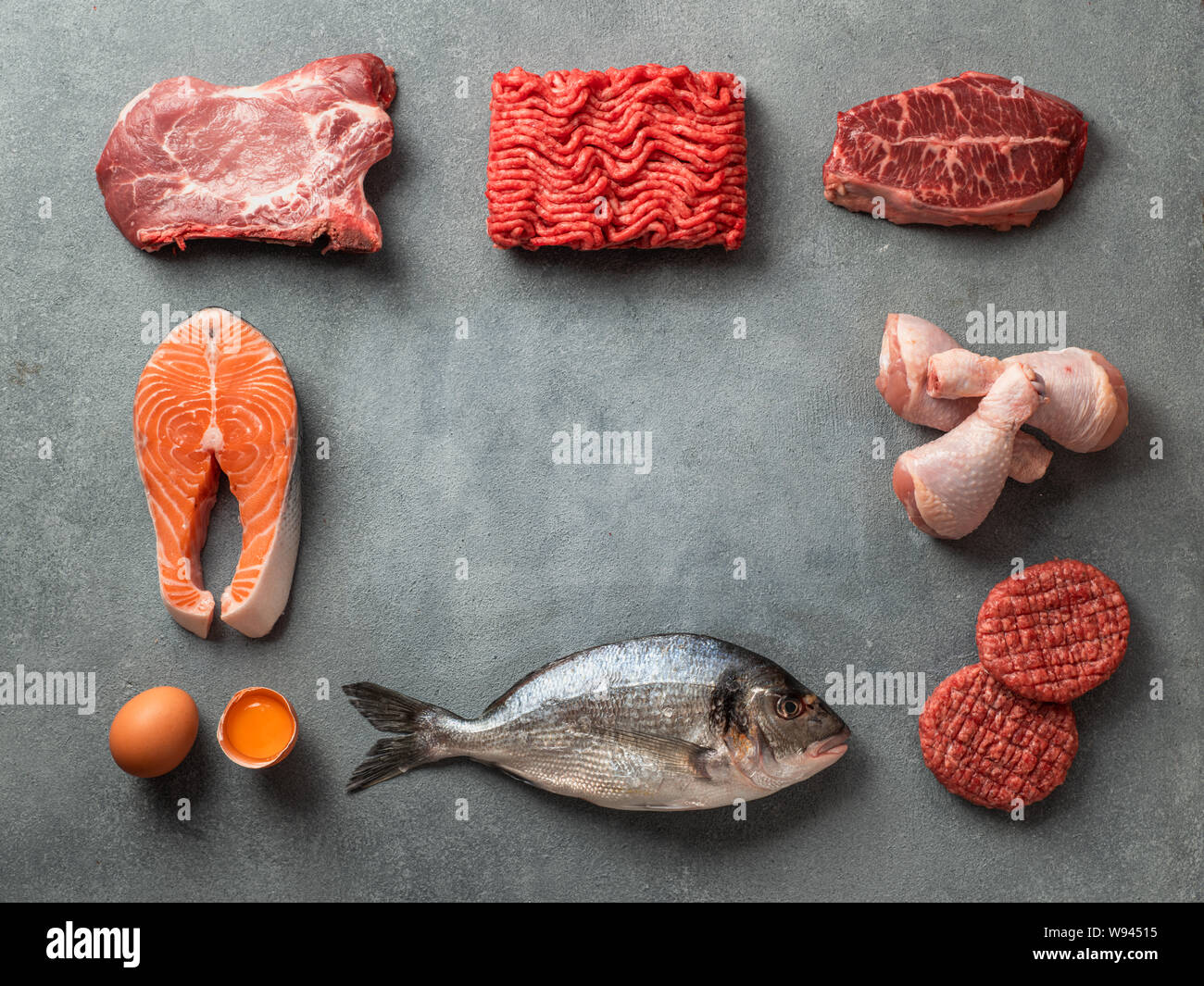 Carnivore or keto diet concept. Raw ingredients for zero carb or low carb diet - meat, poultry, fish, eggs and copy space in center on gray stone back Stock Photo