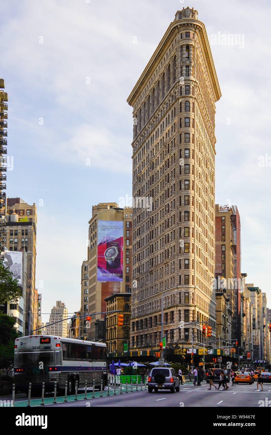 The iconic Flatiron Building at Broadway and 5th avenue intersection in Manhattan. Some people crosswalk the avenue. New York City August 2019, USA. Stock Photo