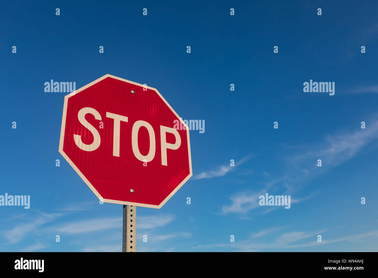 Isolated closeup looking up at red reflective stop sign with blue sky and white clouds in background Stock Photo