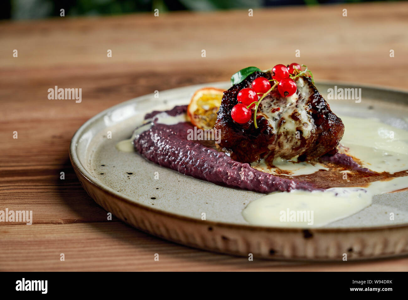Closeup of delicious piece of barbecue staying on plate with vegetable puree, cranberry, mint and lemon. Tasty meal cooked in restaurant in evening. Concept of cuisine and food. Stock Photo
