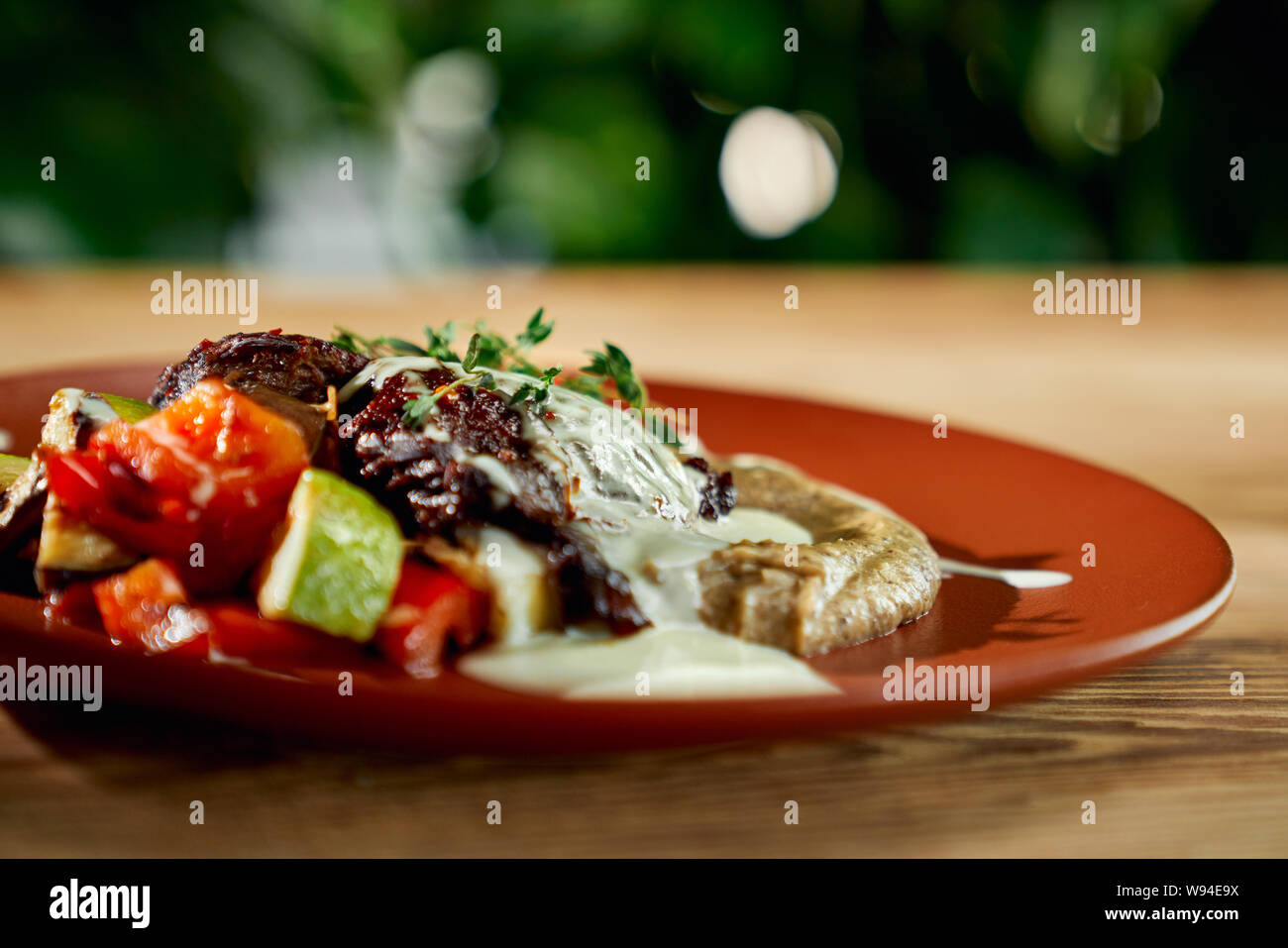 selective focus of delicious juicy meat with garnish and grilled vegetables on plate in restaurant. Healthy meal with marrows and tomatoes staying on table. Concept of dinner and cuisine. Stock Photo
