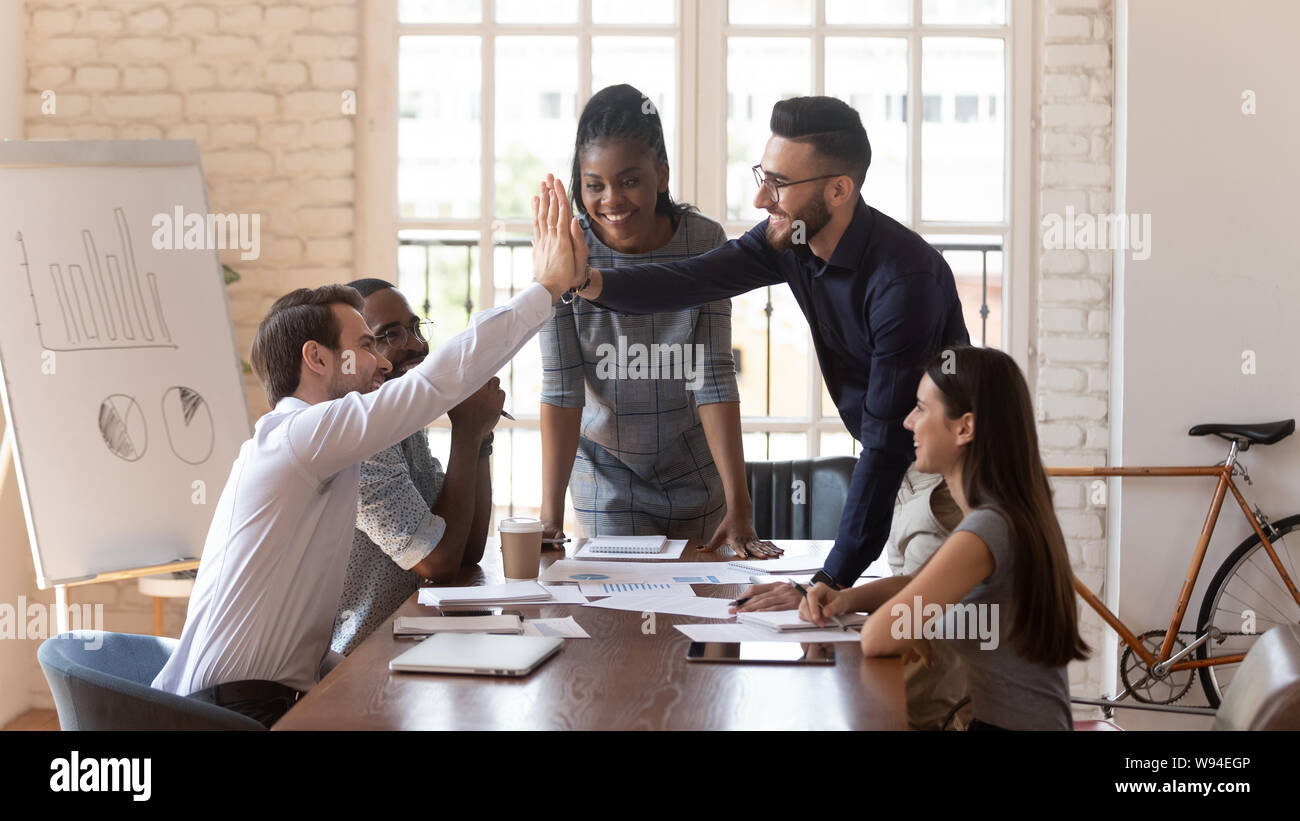 Motivated male colleagues give high five at multiracial group meeting ...