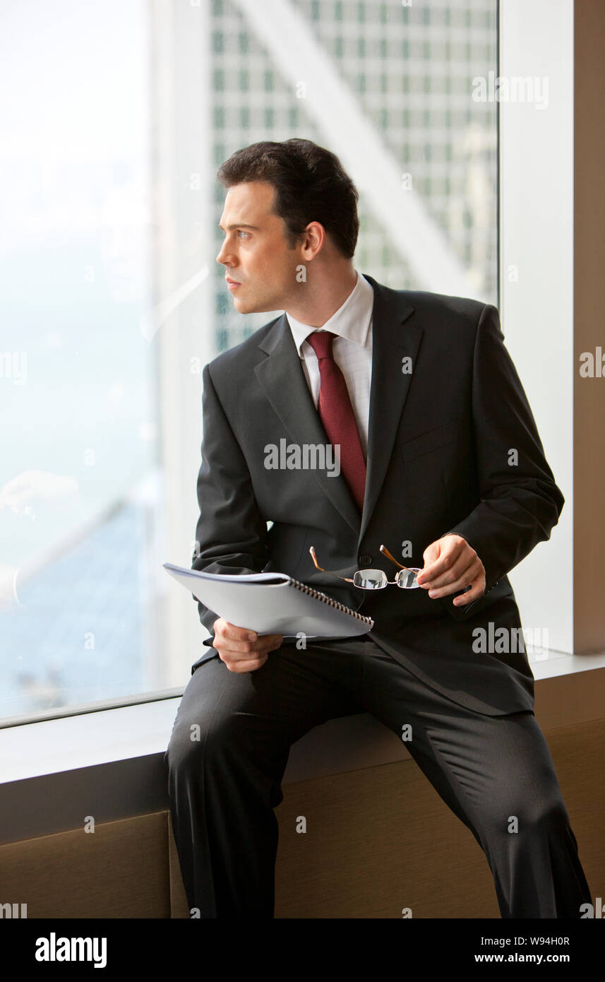 Thoughtful businessman looking through an office building window. Stock Photo