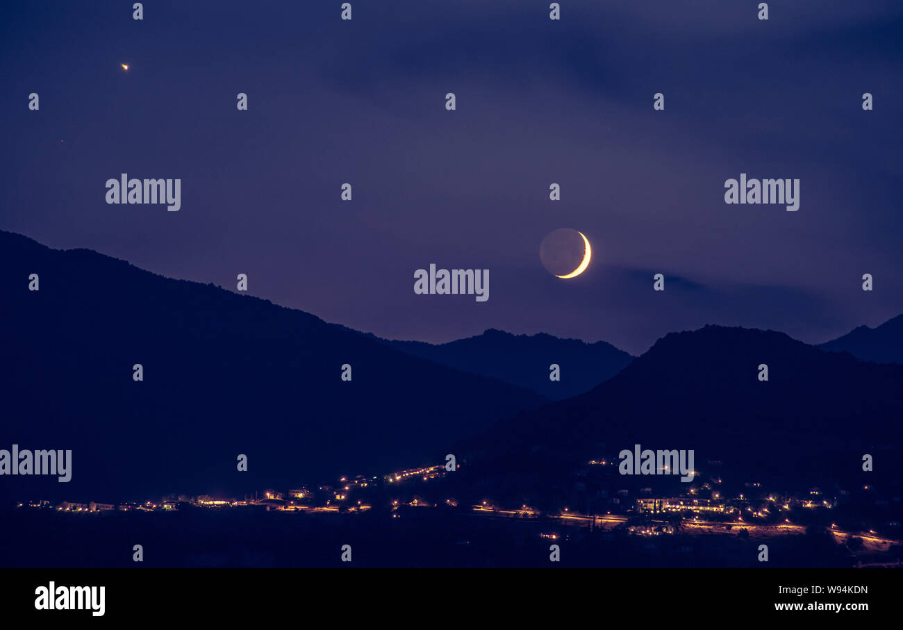 Half moon is rising up on a purple horizon, Mountains and lights from ...