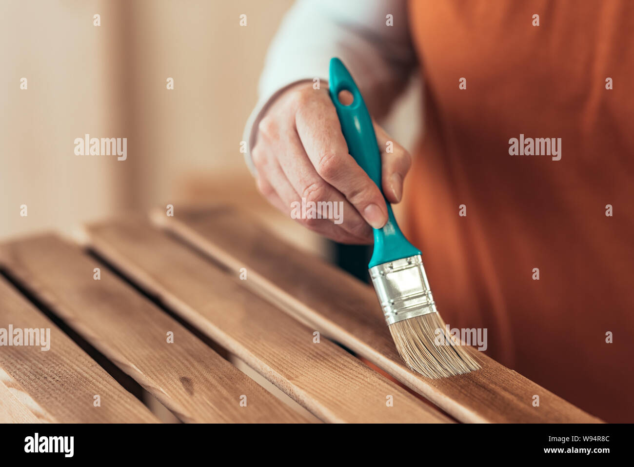 Female carpenter varnishing wooden crate with brush in her small business woodwork workshop Stock Photo