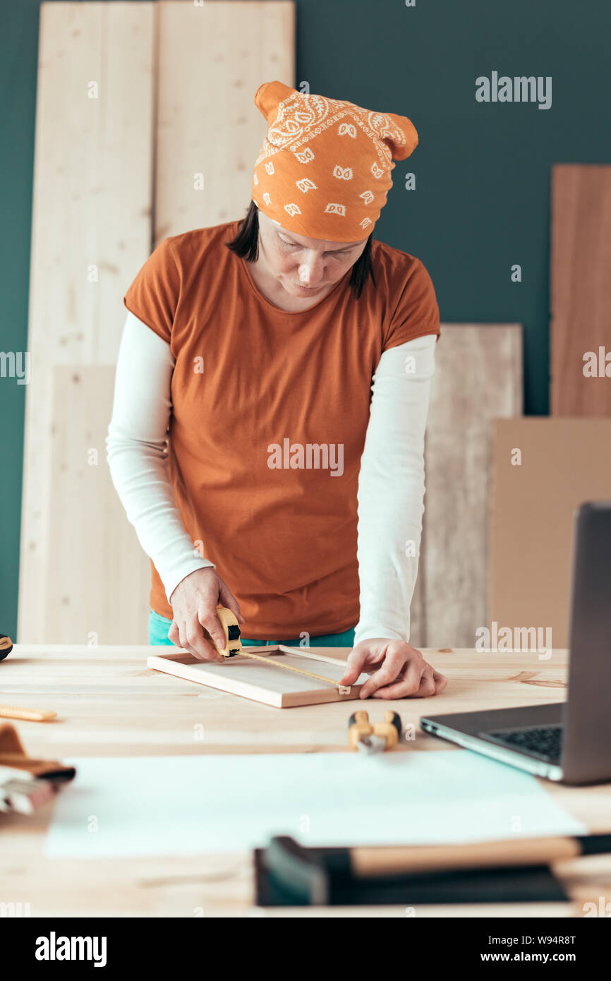 Female carpenter tape measuring picture frame in small business woodwork workshop Stock Photo