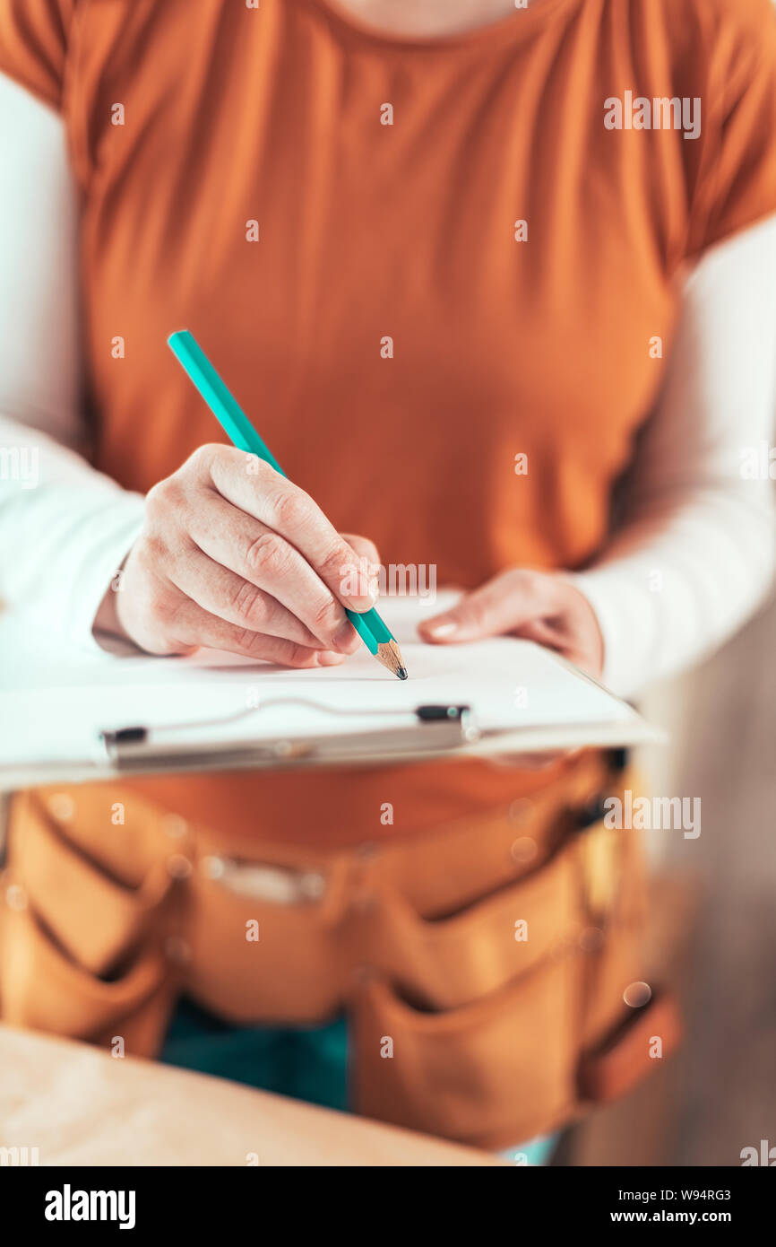 Self employed female carpenter writing project notes on clipboard notepad paper in small business woodwork workshop Stock Photo