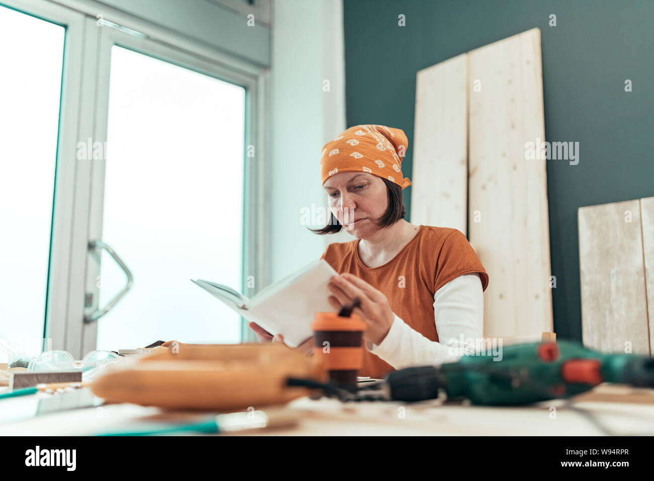 Female carpenter reading DIY project instruction manual in small business woodwork workshop Stock Photo