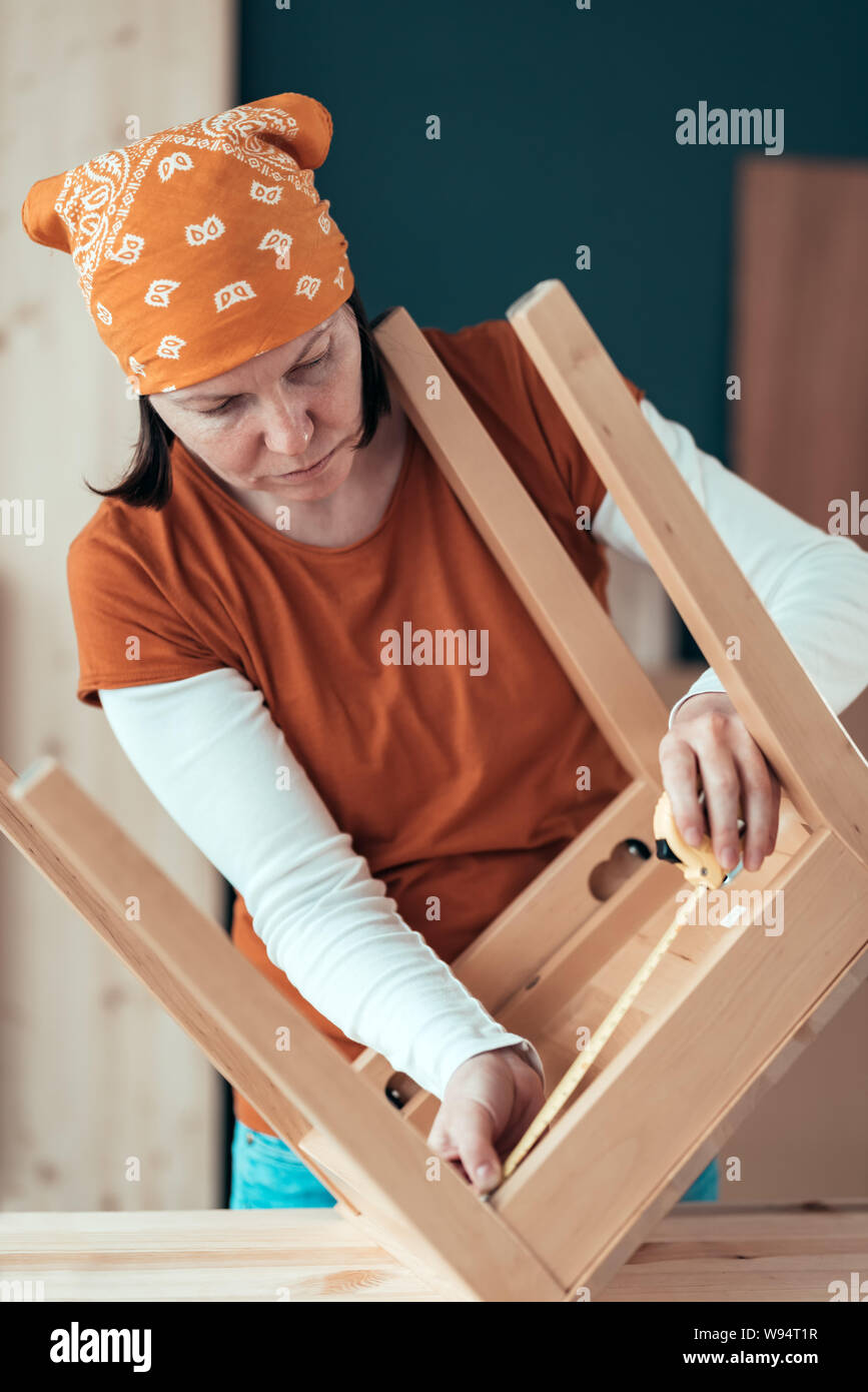 Female carpenter tape measuring wooden chair seat in small business woodwork workshop, close up of hands, selective focus Stock Photo