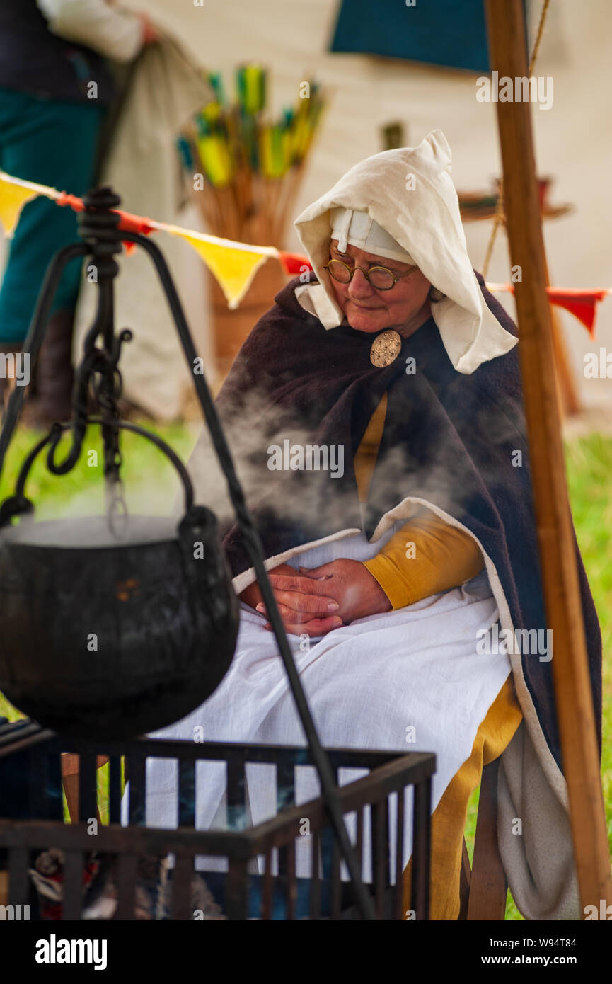 Re-enactors stage the Battle of Shrewsbury 1403 on the original battlefield in July 2019 woman in medieval dress in camp setting with cauldron Stock Photo