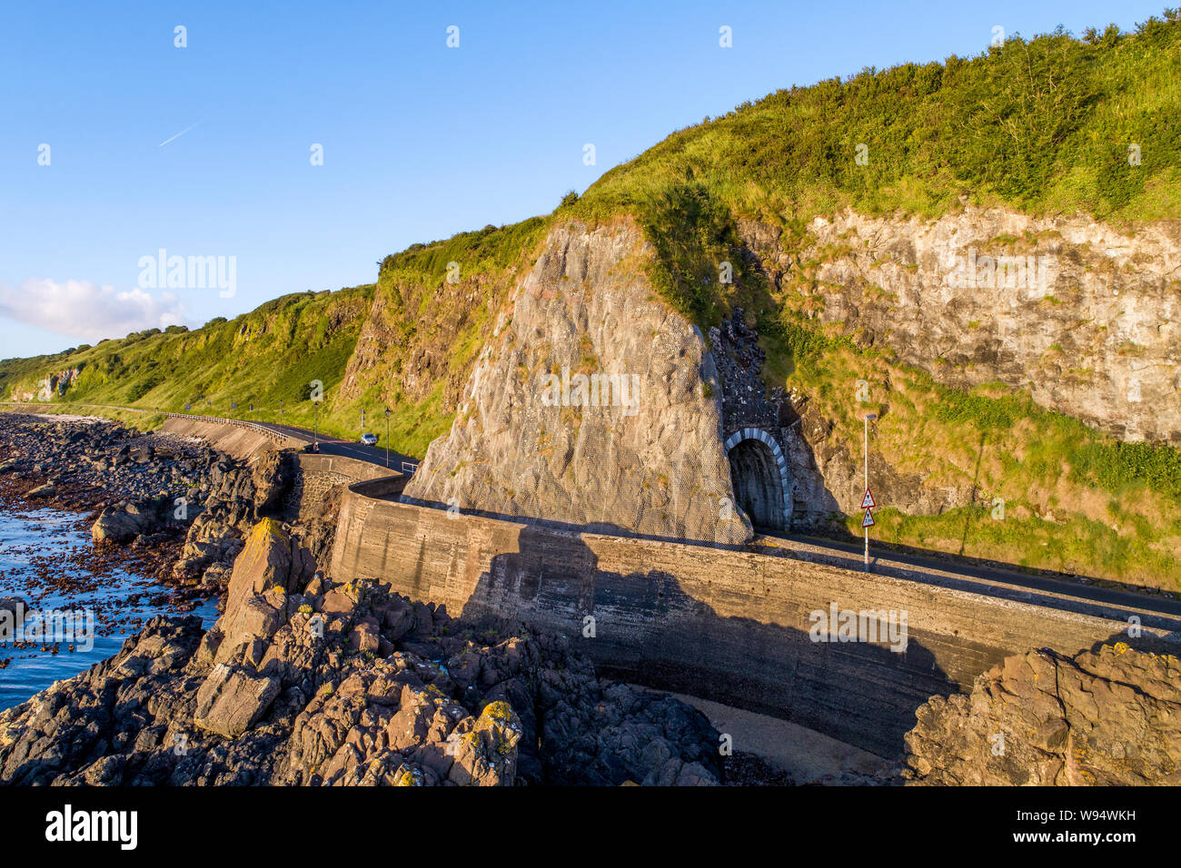 Black Arc tunnel  and Causeway Coastal Route. Scenic road along eastern coast of County Antrim, Northern Ireland, UK. Aerial view in sunrise light Stock Photo