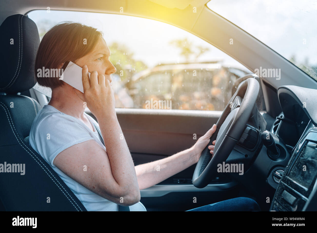 Woman driving car offroad and talking on mobile phone, side view from