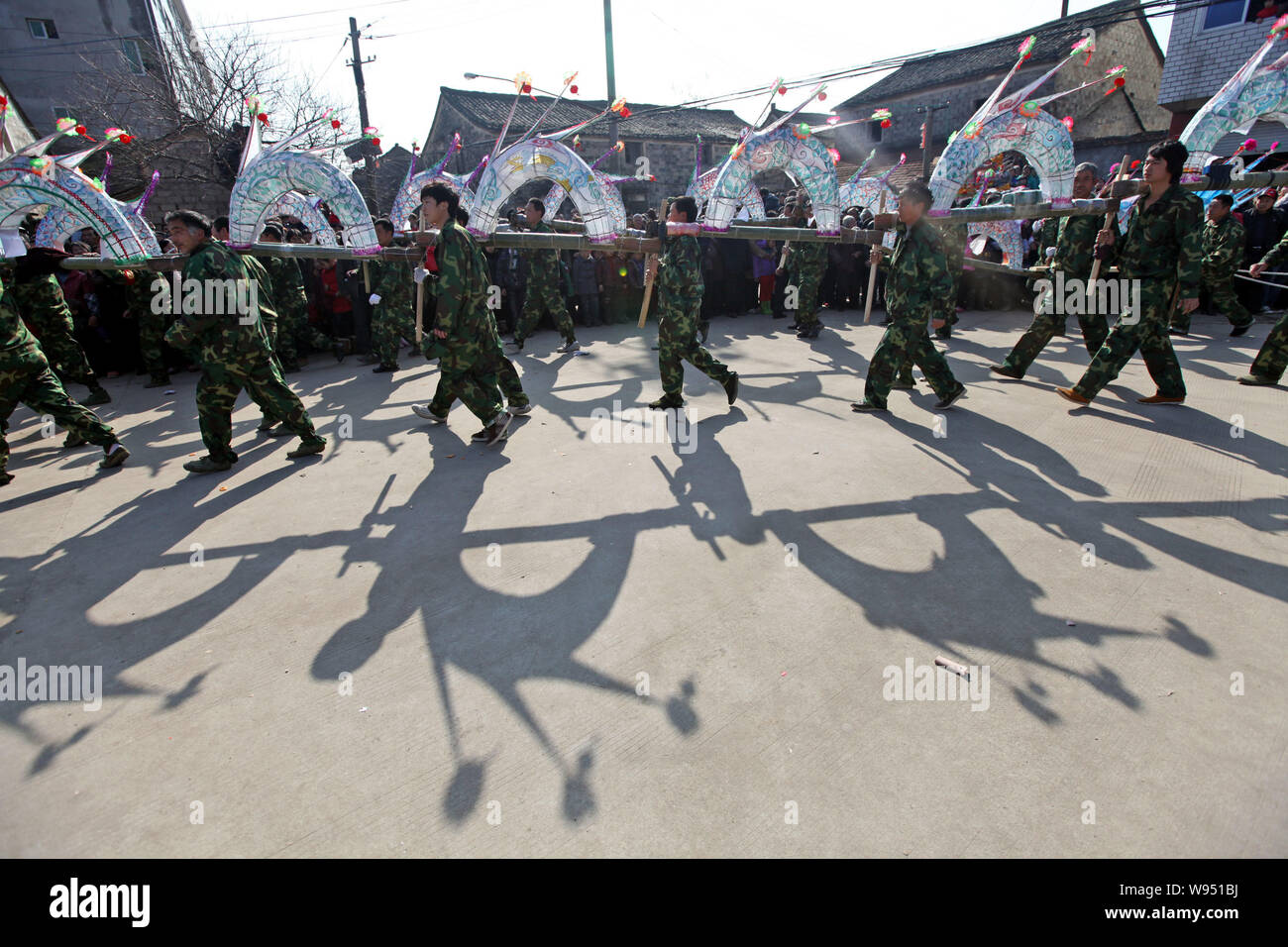 Local Chinese villagers perform a dragon dance with a long bamboo dragon decorated with lit lanterns to celebrate the forthcoming Lantern Festival on Stock Photo