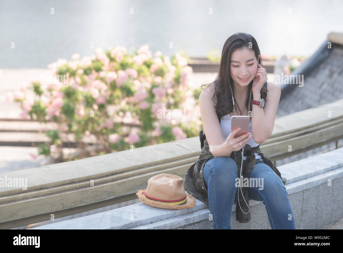 Beautiful asian solo tourist woman relaxing and enjoying listening the music on a smartphone in urban city downtown. Vacation travel in summer. Stock Photo