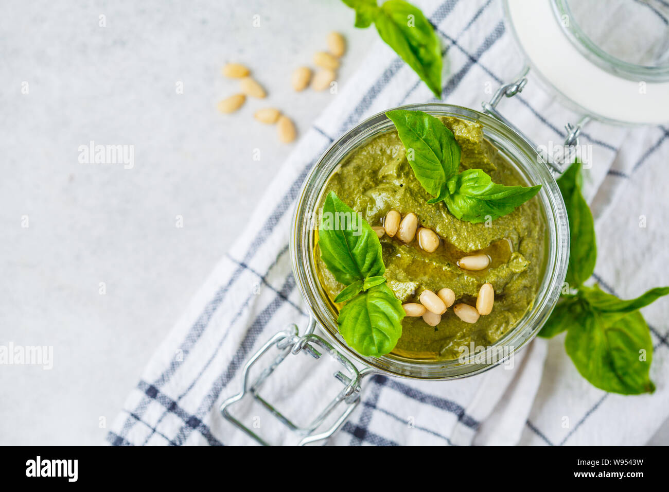 Basil pesto with nuts in a glass jar, top view. Plant based food