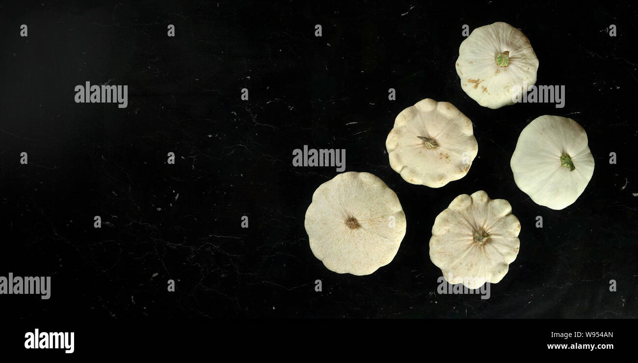 Five white pattypan squash on black marble like board, view from above, wide banner with space for text left side Stock Photo