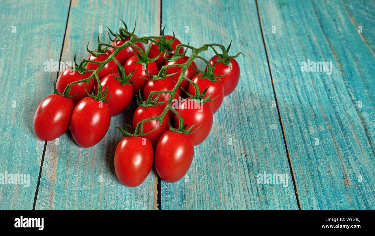 Group of fresh red tomatoes with green stem vines, on wooden boards painted blue, space for text right side Stock Photo